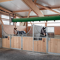 Lubratec Tube Cool aan het plafond van een paardenstal en boven twee paardenboxen met paarden