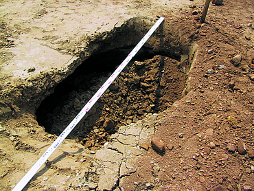 A large hole in the ground is measured using a folding rule