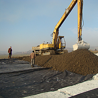 Graafmachine aan het werk, grond verspreiden over het gelegde Basetrac® Woven wapeningsweefsel