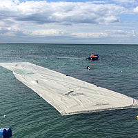 Voorgemonteerde en nog niet gevulde slang uitgespreid op het water en klaar voor installatie in het water