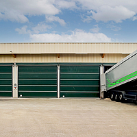 Vier groene poorten op een hal. Een vrachtwagen met materiaal eindigt bij één poort