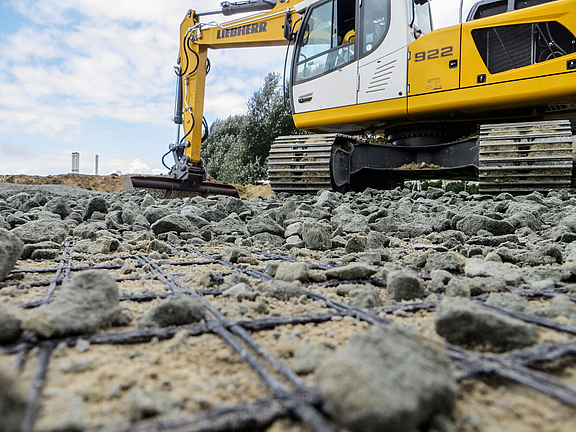 Versterking van de funderingslaag met geogrids Een graafmachine verspreidt bulkmateriaal over het gelegde geogrid