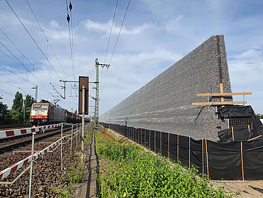 Schienen mit Zug und angrenzend Lärmschutzwand