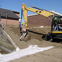 Graafmachine verspreidt grond over Tektoseal® Clay bentonietmatten om een kleine helling te stabiliseren