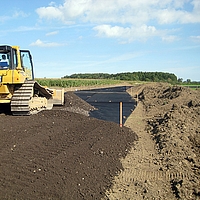 Bulldozer verspreidt grond over een reeds gelegd Basetrac raster op de bouwplaats