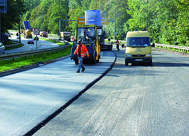 A motorway riddled with potholes, with workers and construction machinery.
